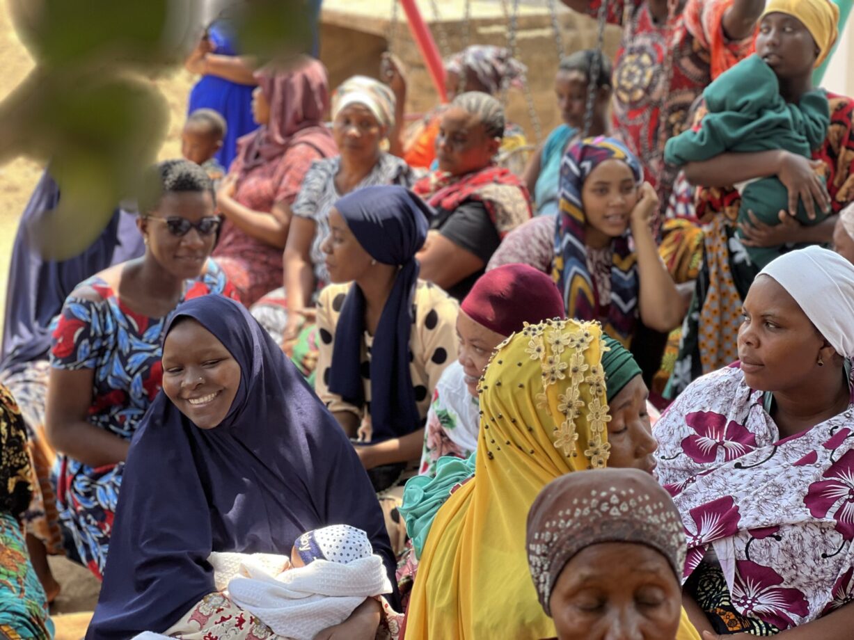 Smiling Maasai women in traditional colorful beaded jewelry and red shuka clothing welcoming volunteers with warm greetings
